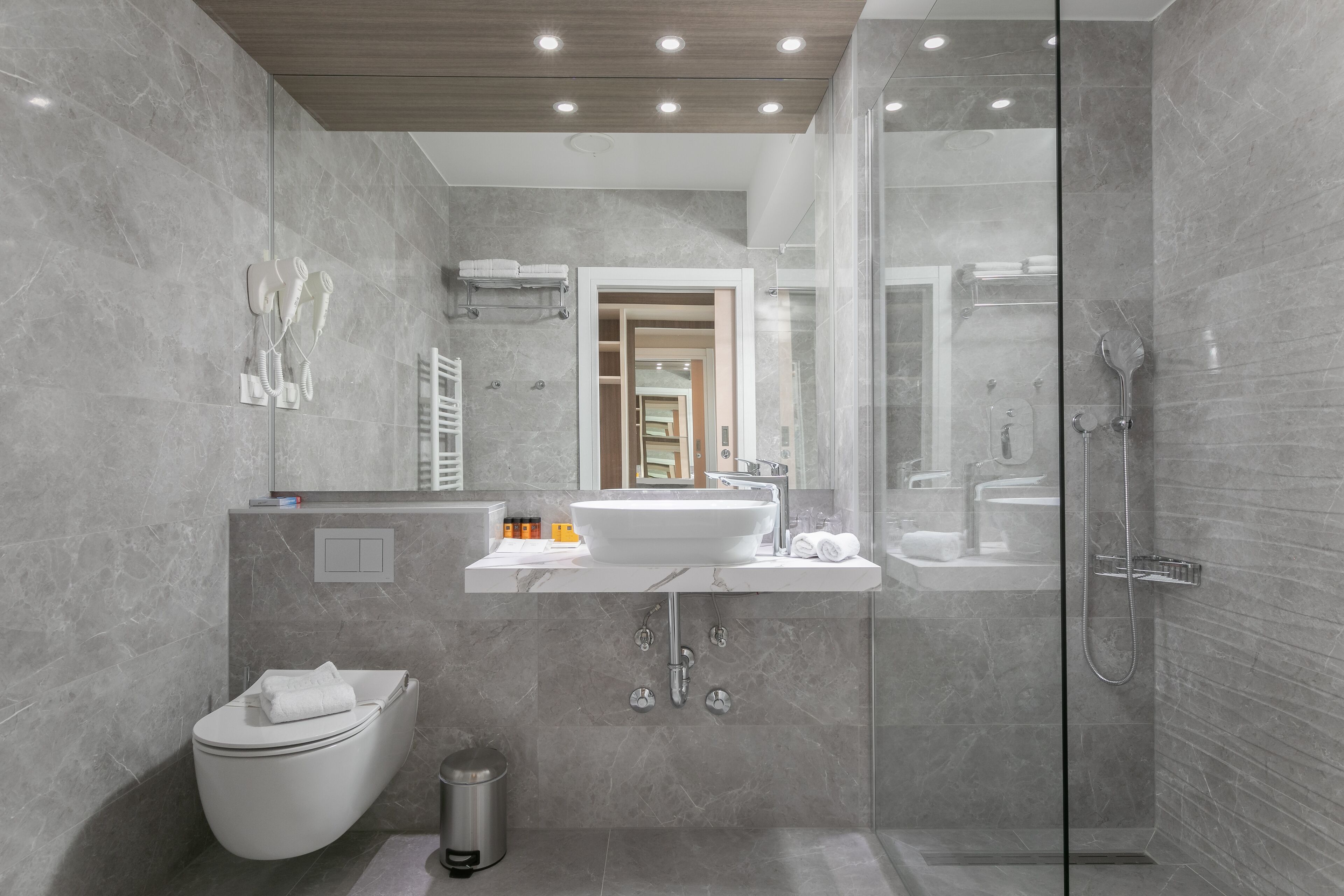Un baño moderno con ducha envuelta en vidrio, un lavamanos blanco y un inodoro.
