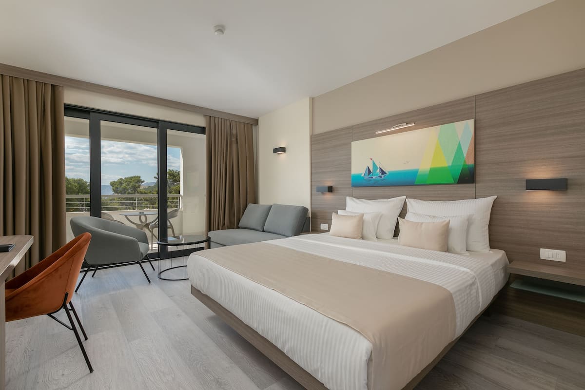 A modern hotel room with a large bed, a seating area with a table, and a view of the outdoors.