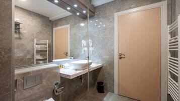 A modern bathroom with a marble wall, a white sink, a large mirror, and a beige door.