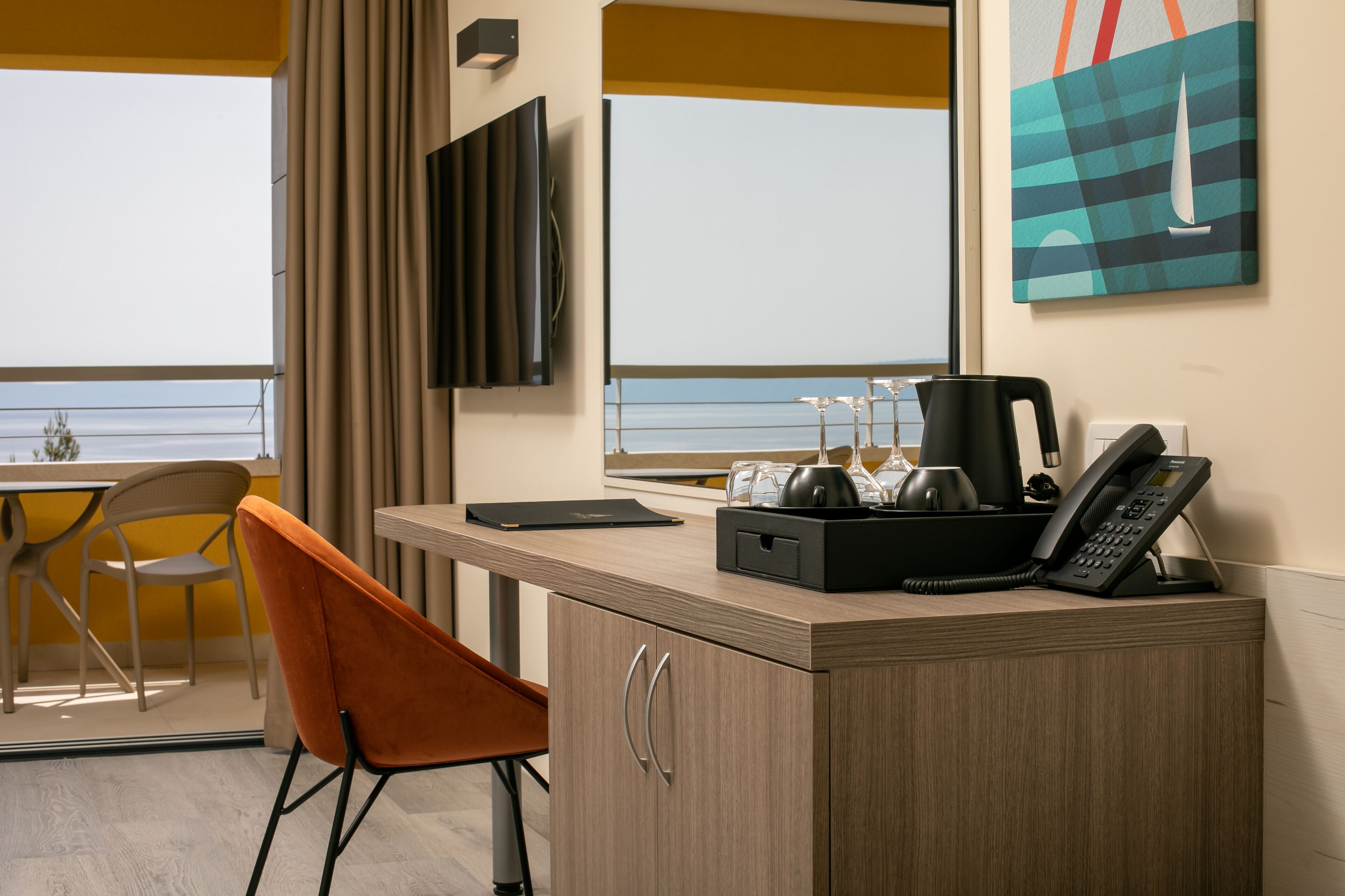 A hotel room with a wooden desk, a chair, a telephone, a coffee maker, and a glass set.