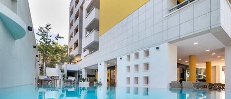 A swimming pool with clear blue water, surrounded by white tiled walls and a yellow accent wall. There are lounge chairs and a small table near the pool.