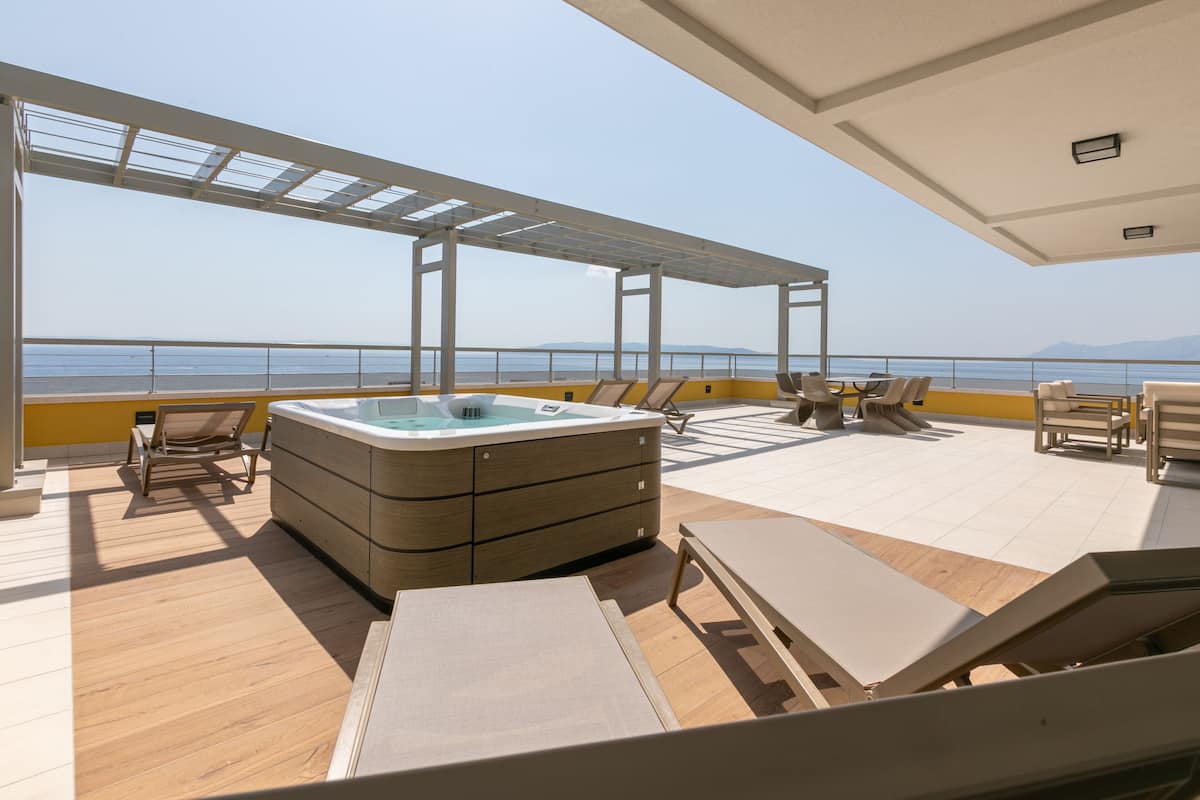 A modern outdoor deck with a hot tub, lounge chairs, and a view of the sea.