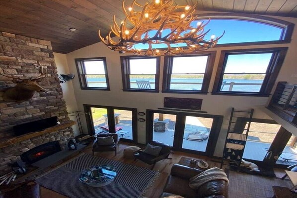 A spacious living area with a stone fireplace, comfortable seating, and large windows offering views of the outdoors.