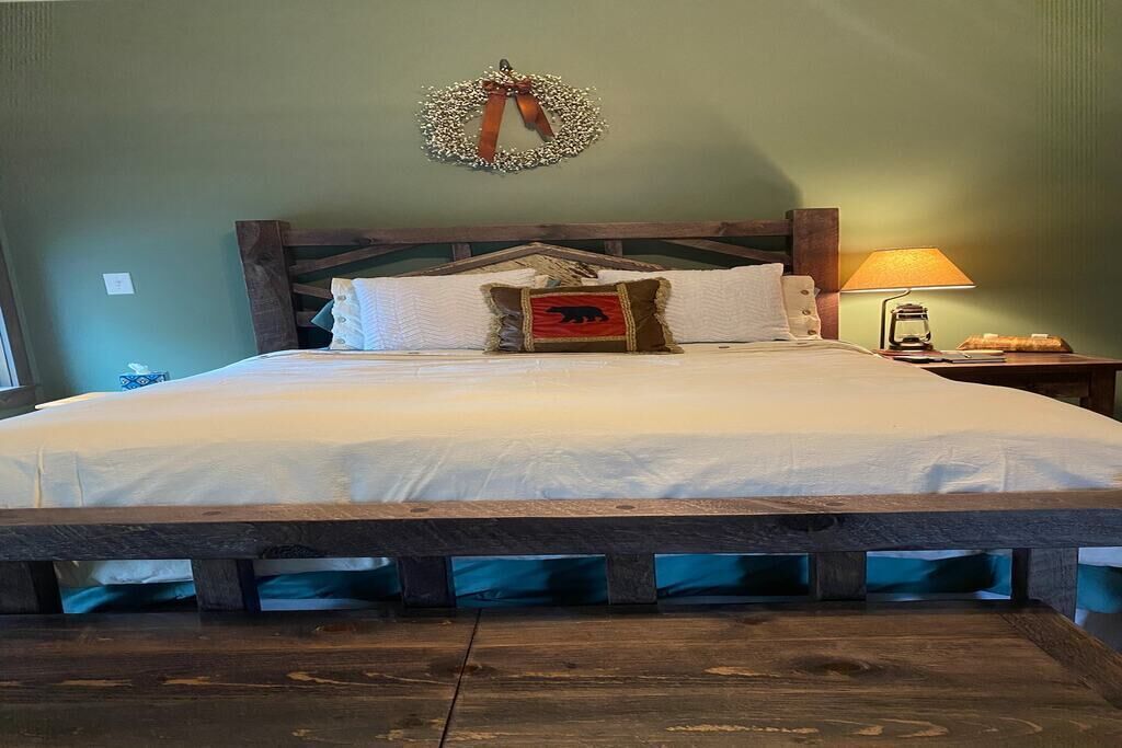 Una cama con cabecera de madera, un adorno en la pared y una mesita de noche con lámpara.