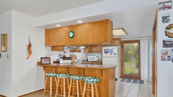 Uma cozinha com armários de madeira, uma ilha central com banquetas, micro-ondas e geladeira.