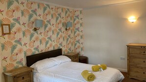 A neatly made bed with white bedding, two wooden nightstands, a wooden dresser, and a wall with a floral pattern. - The Tayleur Arms (Telford)