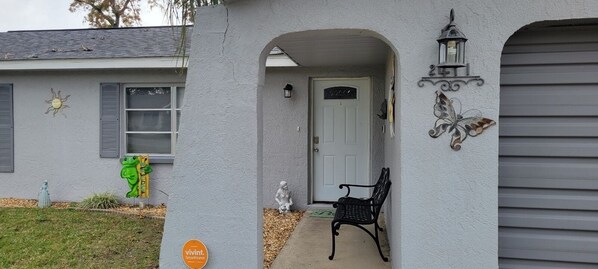 A house with a white exterior, a front door, a bench, and a butterfly decoration.