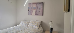 A bedroom with a bed, a nightstand, and a wall-mounted painting.