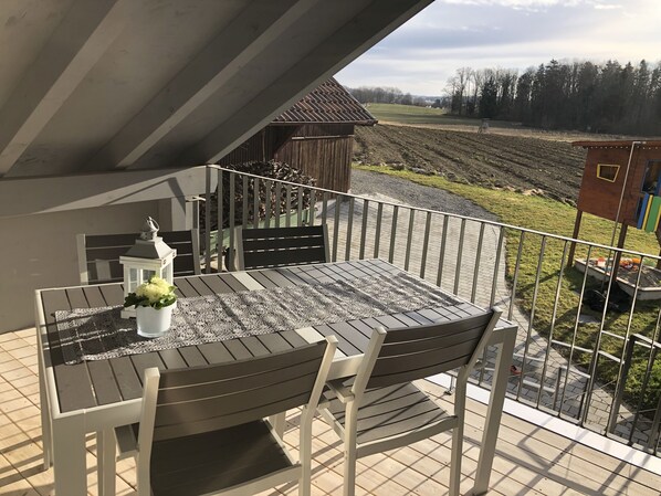 A balcony with a table and chairs, overlooking a field and a small wooden structure. - Cozy vacation apartment in the Lake Constance hinterland (Markdorf)