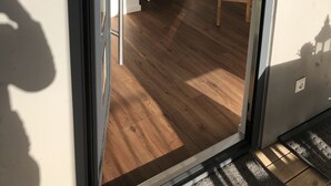 Une pièce dotée d’une lucarne, d’un plancher en bois, d’une petite table blanche ornée d’un vase et d’une échelle en bois.