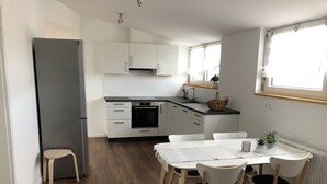 Une cuisine moderne avec des meubles blancs, un plan de travail noir et un coin repas comprenant une table et des chaises blanches.