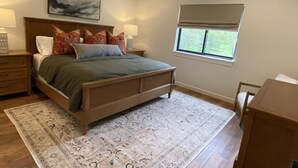 Un dormitorio con cama, mesitas de noche, ventana y vistas a árboles.