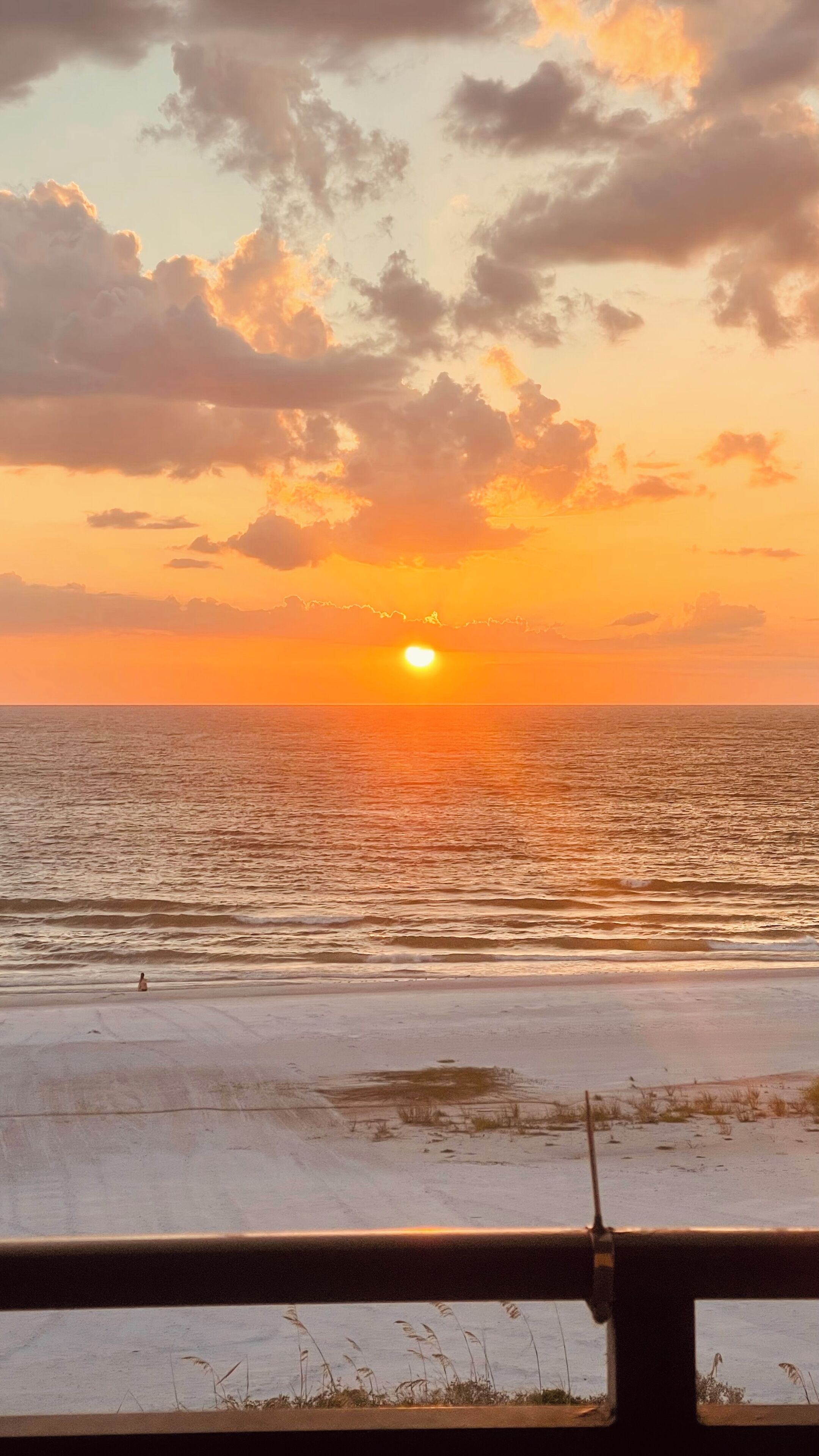 Ein Sonnenuntergang über dem Meer mit einem Strand im Vordergrund.