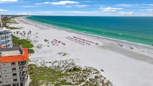 A beach with rows of pink umbrellas and a building with a red roof.