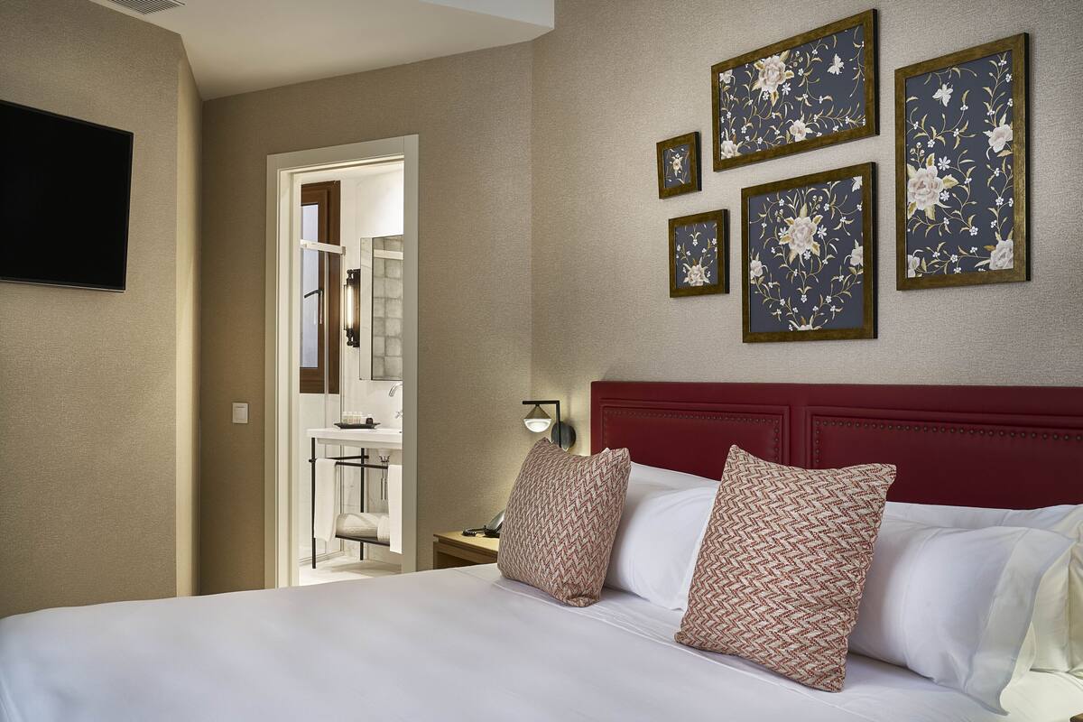 A hotel room with a large bed, a red headboard, and a wall with framed floral artwork.