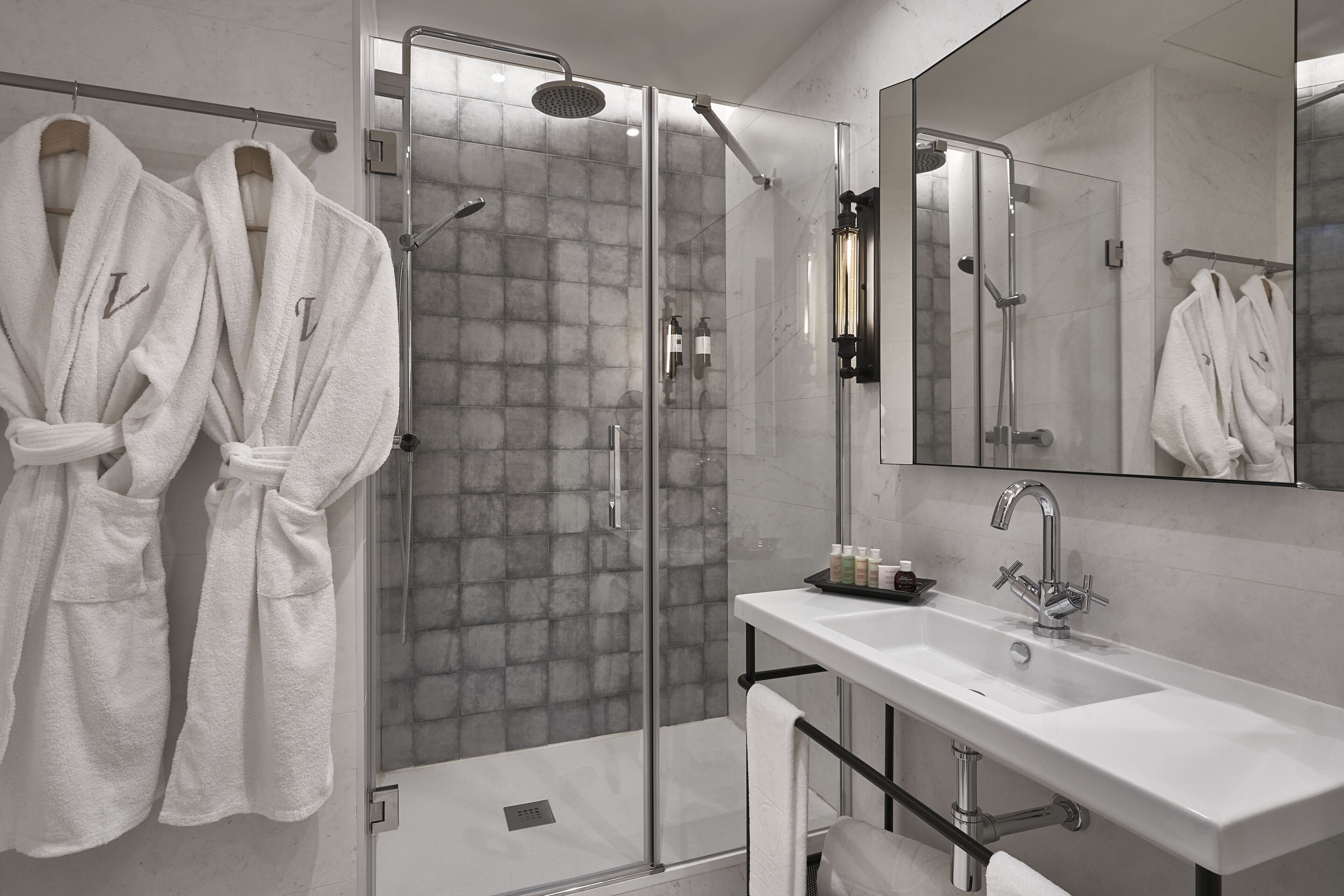 Un baño moderno con ducha envuelta en vidrio, un espejo grande y dos toallas blancas colgadas en ganchos.