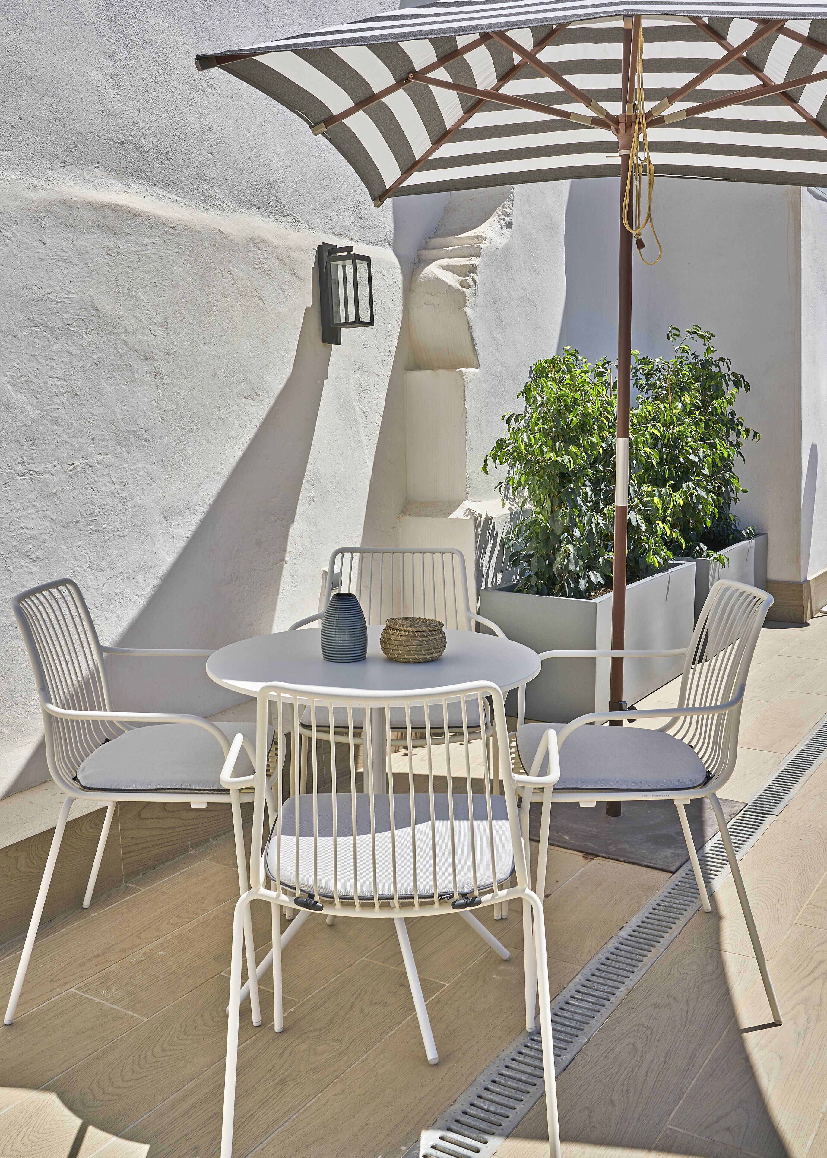 A patio with a round table and four chairs, a striped umbrella, and a potted plant.