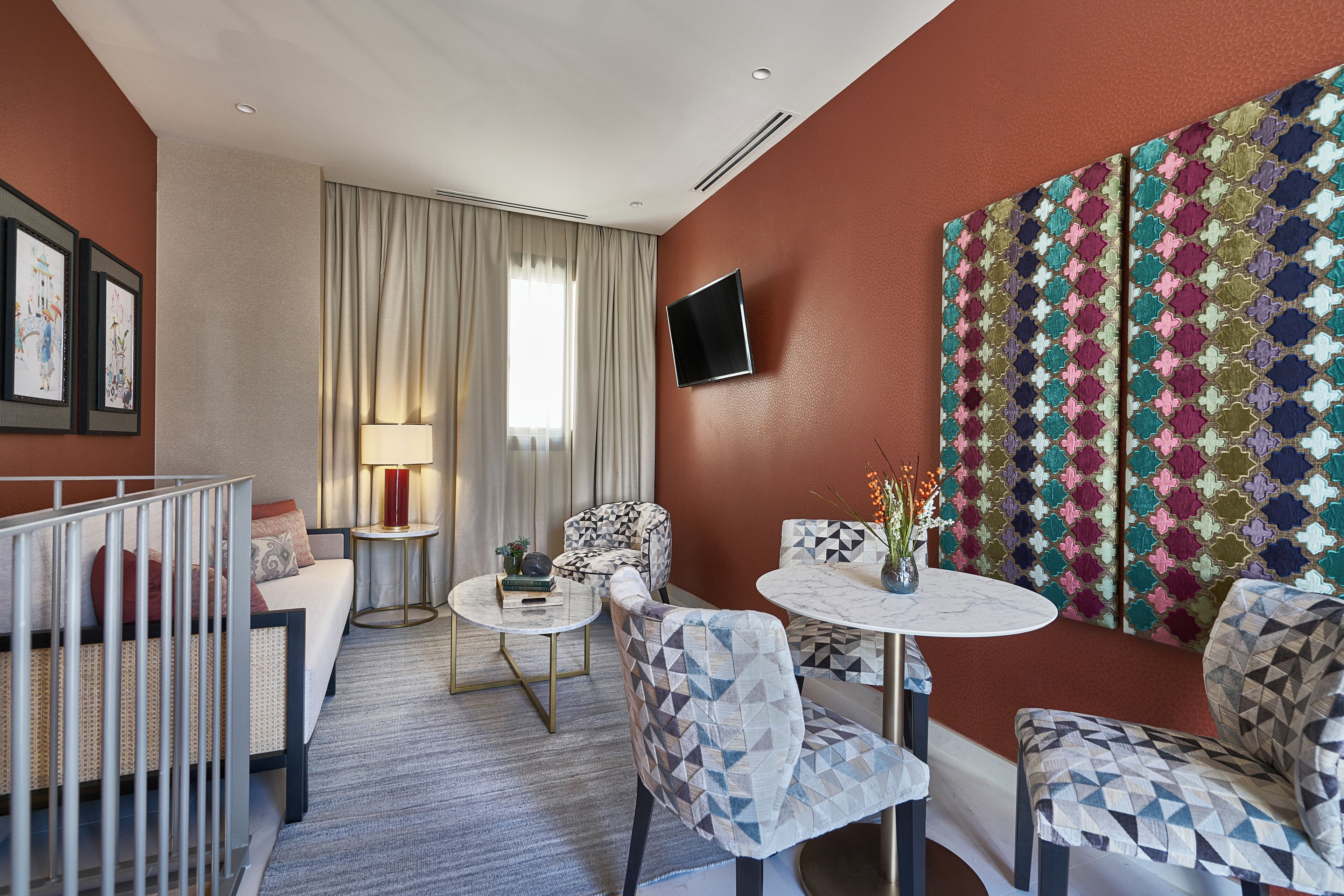 Une chambre d’hôtel comprenant un lit, un coin salon avec une table et des chaises, une grande fenêtre avec des rideaux et une décoration murale colorée.
