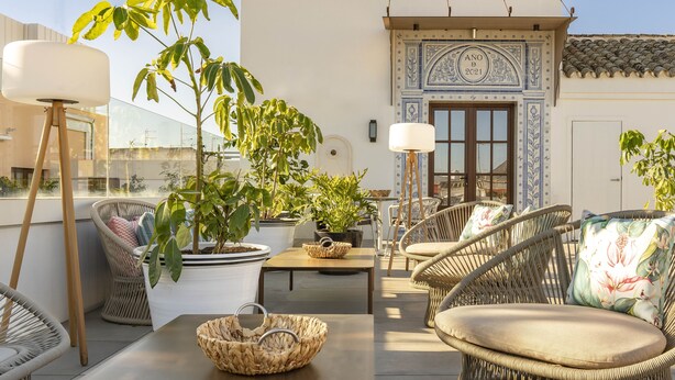 A rooftop terrace with wicker furniture, potted plants, and a decorative wall.