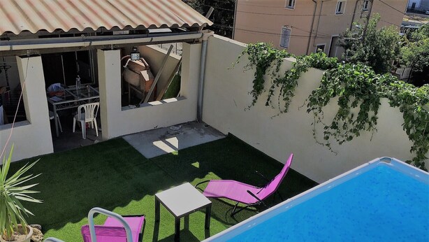 A backyard with a swimming pool, a small patio area with a table and chairs, and a covered outdoor seating area. - Comme à La Maison (Ales)