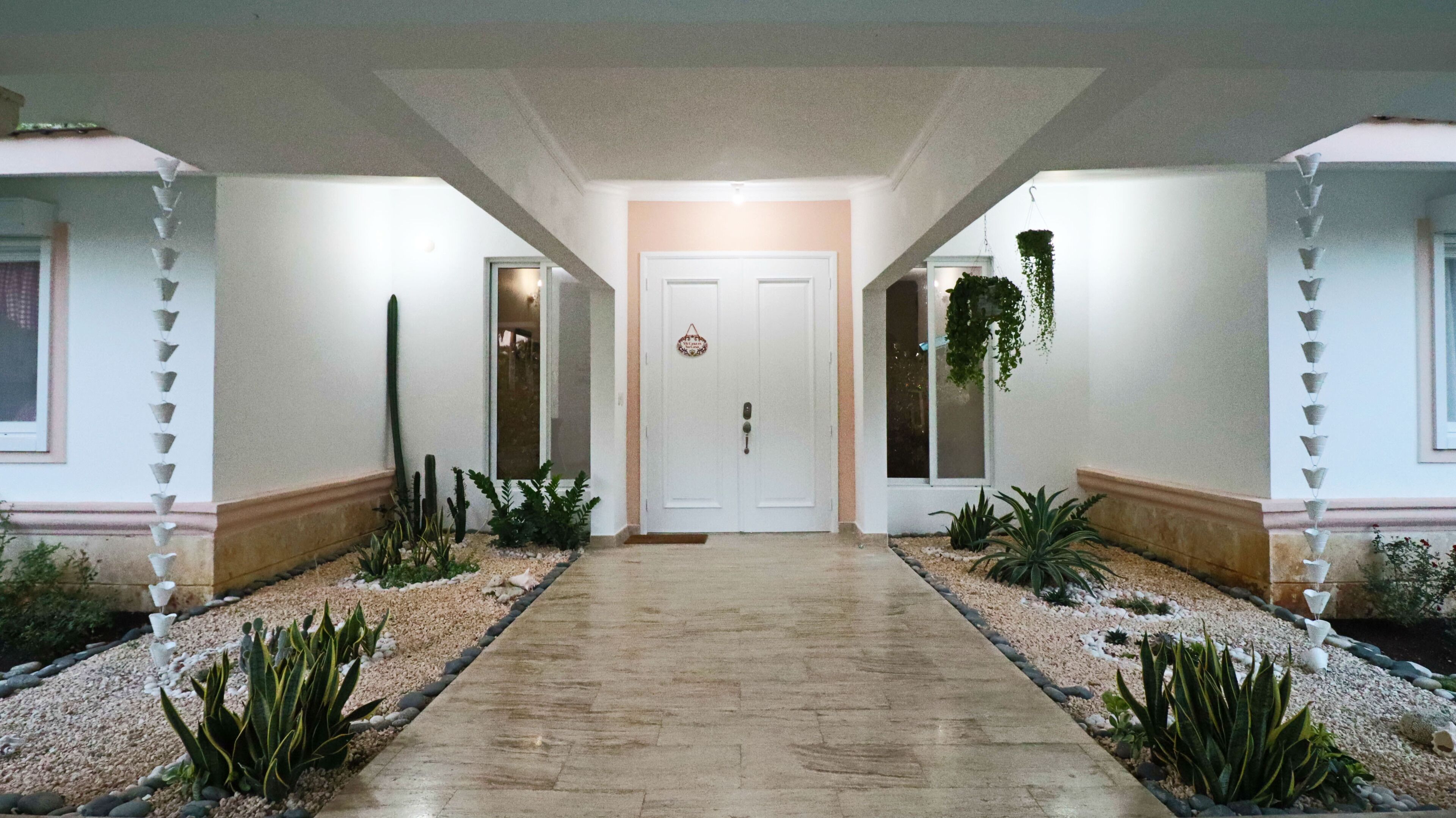 Un pasillo con piso de baldosas, una puerta blanca al final y plantas a ambos lados.
