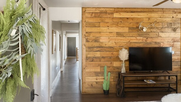 Un salón moderno con pared de madera, televisor de pantalla plana, ventilador de techo y planta en maceta.