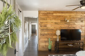 Un salón moderno con pared de madera, televisor de pantalla plana, ventilador de techo y planta en maceta.