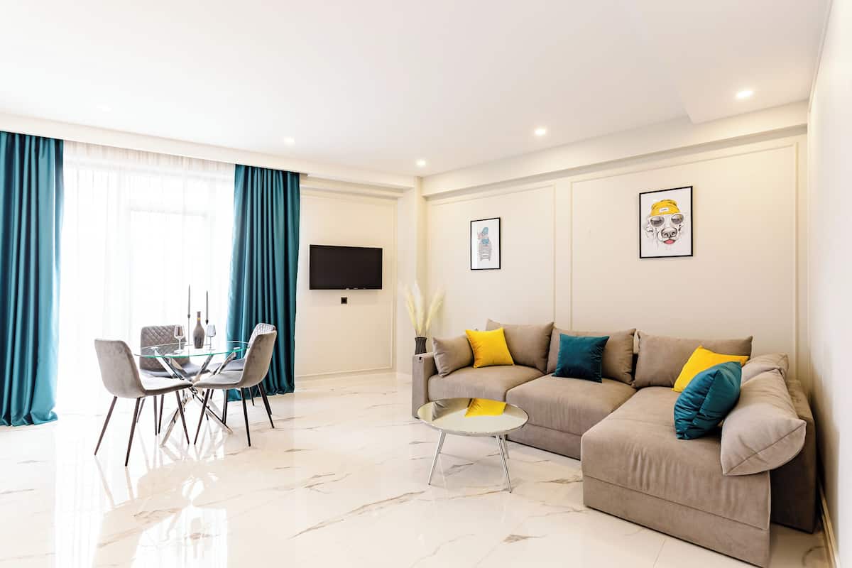 A modern living room with a sofa, a glass dining table, and a TV mounted on the wall.
