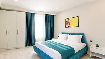 A modern bedroom with a large bed, white wardrobe, teal curtains, and a painting on the wall.
