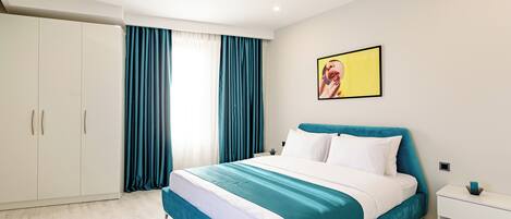 A modern bedroom with a large bed, white wardrobe, teal curtains, and a painting on the wall.