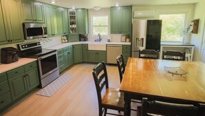 A kitchen with green cabinets, a wooden dining table, and a window. - 6BR Cozy Farmhouse Retreat w/ Sunset Views & Fun
Minutes from Train to Seattle (Sumner)
