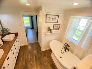 Une salle de bain avec une grande baignoire, un lavabo et un espace douche. Un panneau est accroché au mur avec l’inscription suivante : « Bain chaud : LAVEZ-VOUS, DÉTENTE, RELAXATION ».