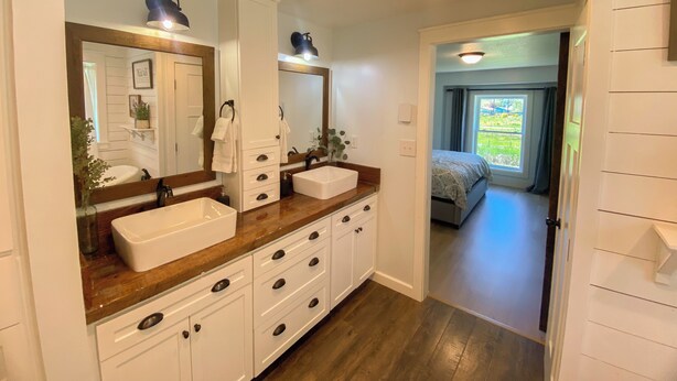 A bathroom with two sinks, a large mirror, wooden vanity, and a view to a bedroom. - 6BR Cozy Farmhouse Retreat w/ Sunset Views & Fun
Minutes from Train to Seattle (Sumner)