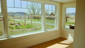 A room with large windows offering a view of a rural landscape, including a road and trees. - 6BR Cozy Farmhouse Retreat w/ Sunset Views & Fun
Minutes from Train to Seattle (Sumner)