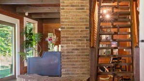 A rustic interior with a brick fireplace, wooden bookshelves, and a staircase. - Cabin on the Crook: private, pet friendly residence alongside a nature preserve (Rising Fawn)