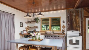A kitchen with a large island, wooden stools, a white stove, and a window with a view of greenery. - Cabin on the Crook: private, pet friendly residence alongside a nature preserve (Rising Fawn)