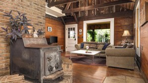 A rustic living room with a stone fireplace, wooden beams, a sofa, and a television. - Cabin on the Crook: private, pet friendly residence alongside a nature preserve (Rising Fawn)