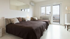 Ein modernes Schlafzimmer mit zwei Betten, einem großen Spiegel und Blick auf die Stadt durch große Fenster.