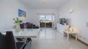 Una sala de estar moderna con una mesa de comedor de vidrio, un sofá, un televisor y un balcón con vista a la ciudad.