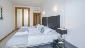 Una habitación de hotel moderna con una cama grande, una mesita de noche, una lámpara de pared y un equipo de aire acondicionado.