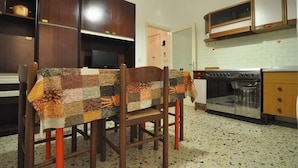 A kitchen with wooden cabinets, a stove, and a table covered with a patchwork tablecloth. - A few steps from the sea (Marina di Grosseto)