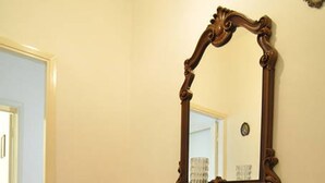 A wooden dresser with a mirror in a hallway with a tiled floor and a door in the background. - A few steps from the sea (Marina di Grosseto)