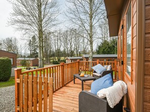 A wooden deck with outdoor furniture, a wooden railing, and a view of the surrounding area including trees and other cabins.