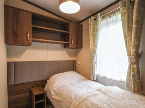 Un dormitorio con cama, armarios de madera, una mesita y una ventana con cortinas estampadas.