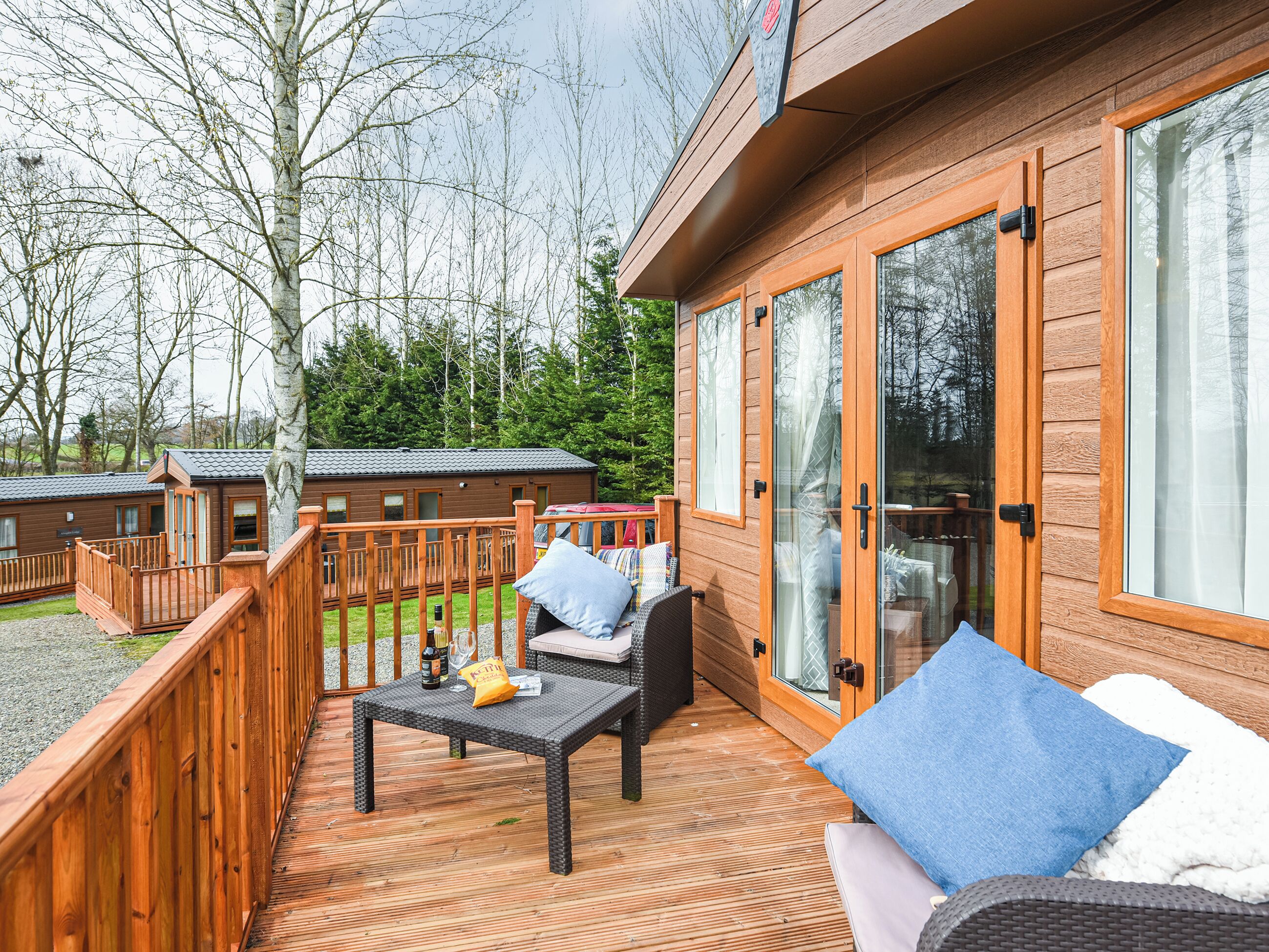 A wooden deck with outdoor furniture, a glass door, and a view of a forested area.
