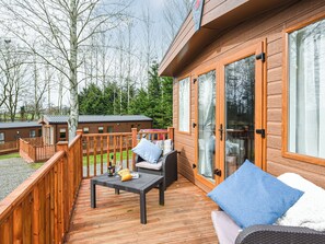 A wooden deck with outdoor furniture, a glass door, and a view of a forested area.