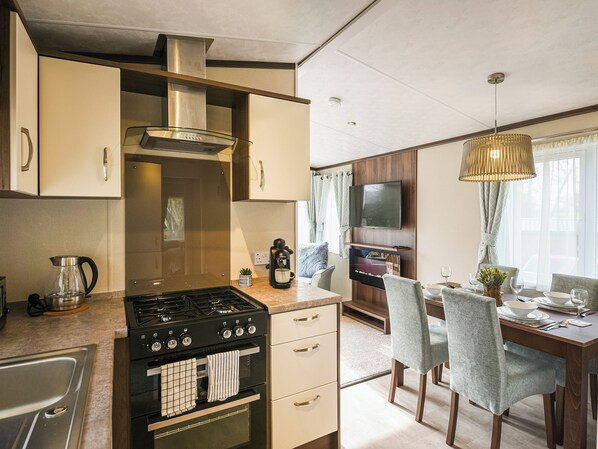 A compact kitchen with a stove, oven, and coffee maker, a dining area with chairs and a table, and a TV mounted on the wall.