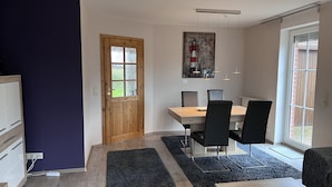 Een eetgedeelte met een houten tafel en zwarte stoelen, een houten deur met glaspanelen en een uitzicht door een groot raam.