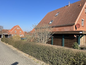 Un quartier résidentiel avec des maisons en briques, une route asphaltée et une haie bien entretenue.