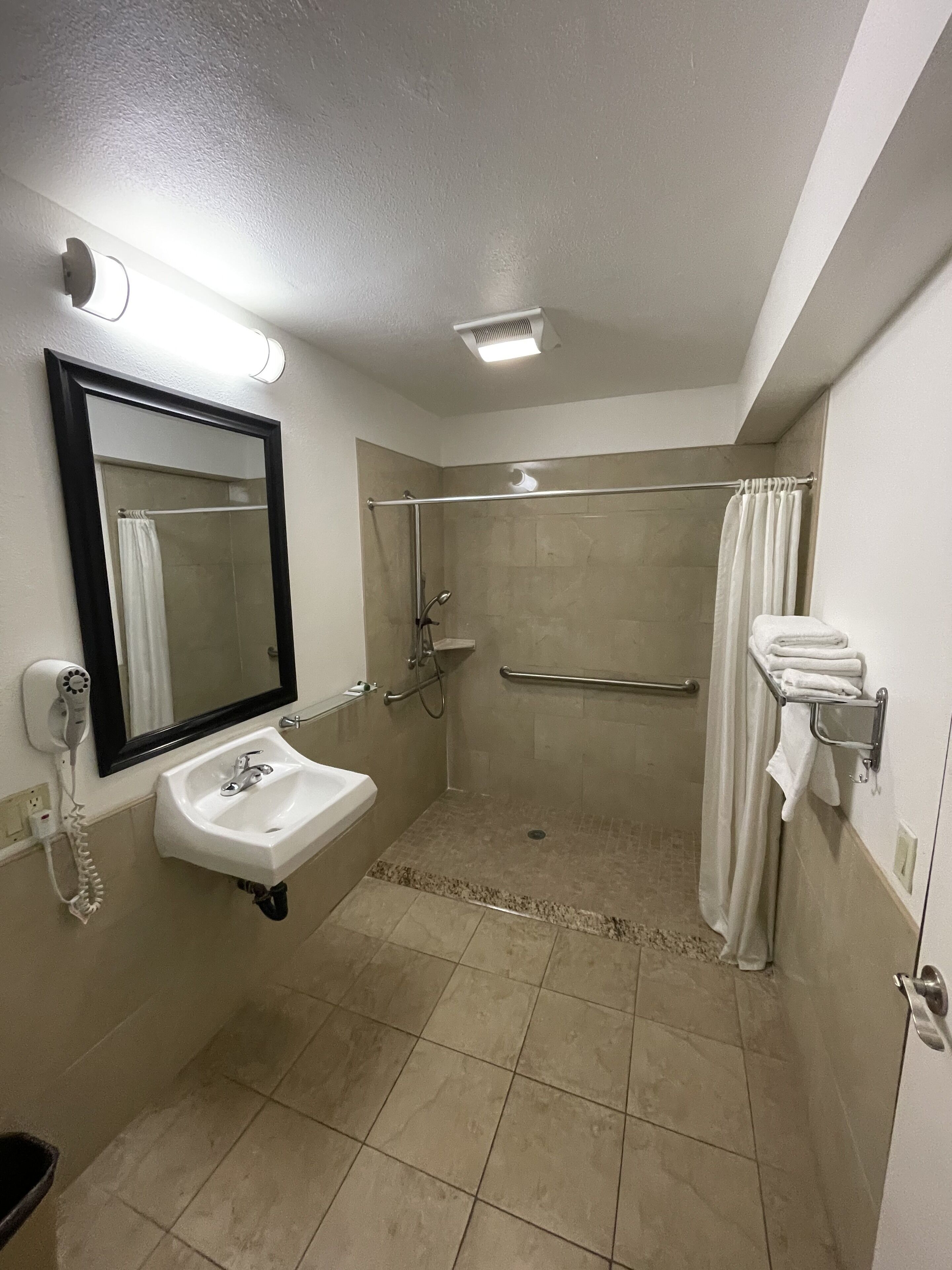Un baño con lavamanos, espejo, ducha y toallero.